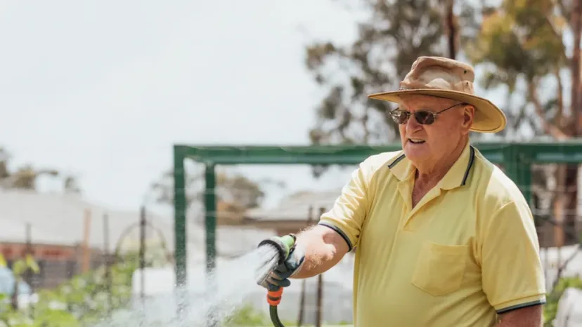 An older man watering plants in his garden.