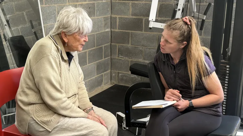 A physiotherapist talking with an older woman in a gym.
