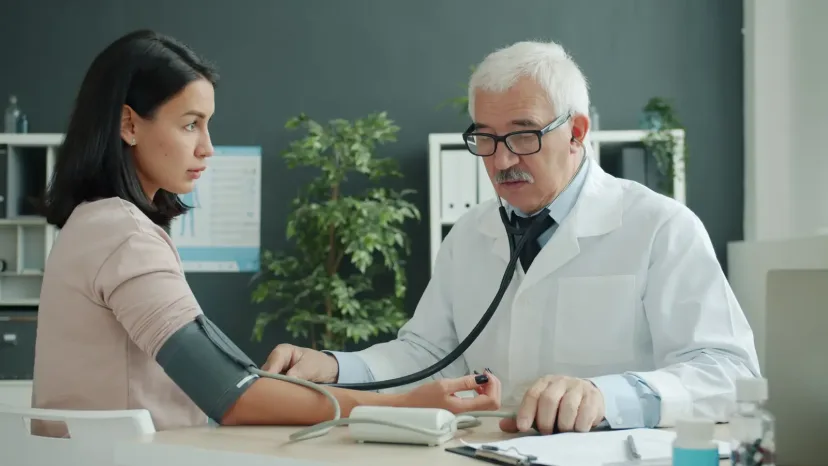 A doctor checking a woman's blood pressure at a clinic desk.