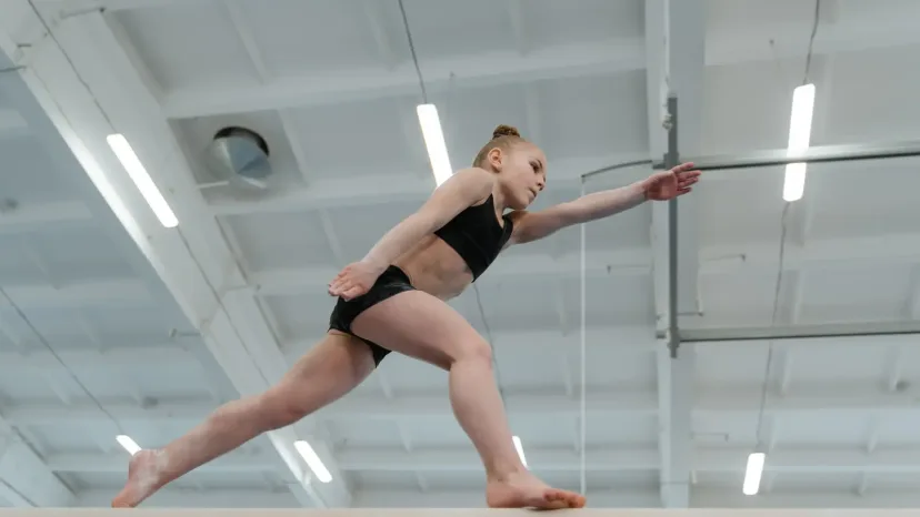 A young gymnast balancing on a beam in a gymnastics hall.
