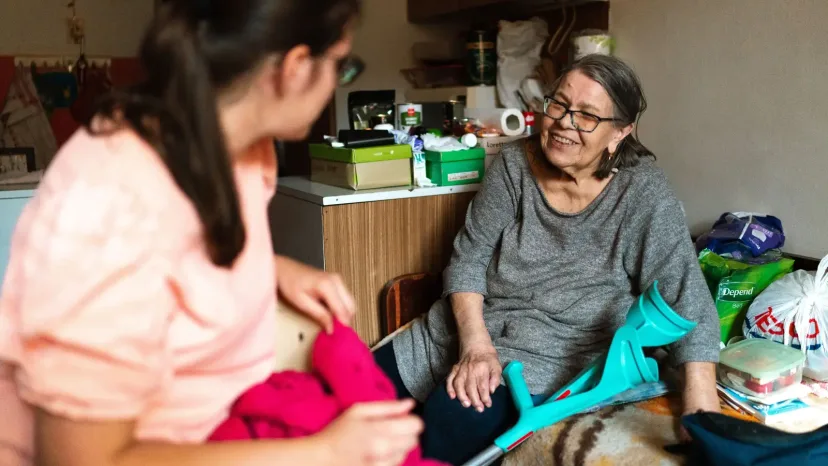 A home carer folding laundry beside a smiling older woman.