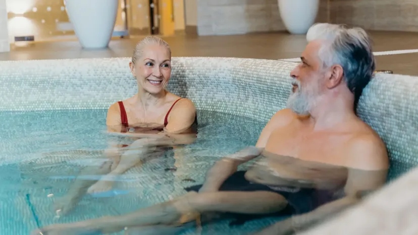 An older couple smiling in a warm indoor hydrotherapy pool.