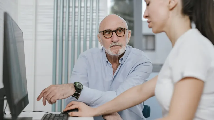 An older man and a younger woman looking at a computer together.