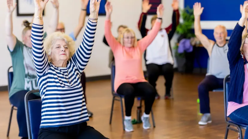 Older women raising their arms in a seated exercise class.